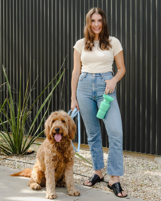 a girl holding a water bottle and a dog drinking water from that bottle