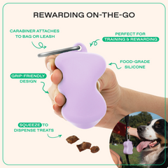 Hand holding lilac silicone treat dispenser with carabiner clip, highlighting grip-friendly design and squeeze-to-dispense features