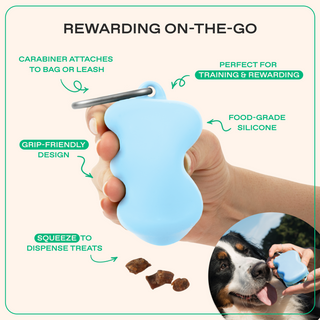 Hand holding sky blue silicone treat dispenser with carabiner clip, highlighting grip-friendly design and squeeze-to-dispense features