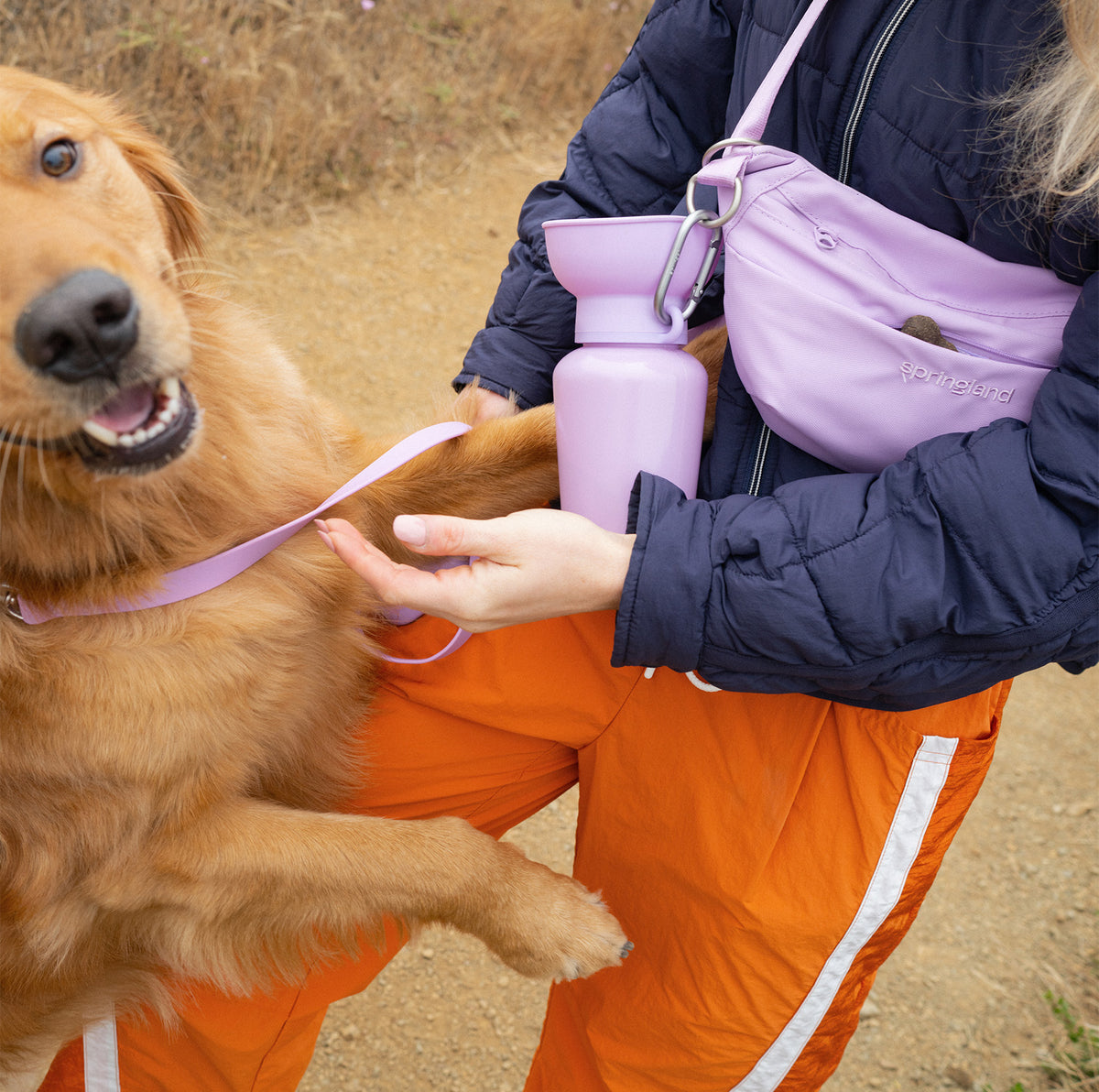Dog mom with a lilac walking bag and water bottle sharing a moment with her golden retriever